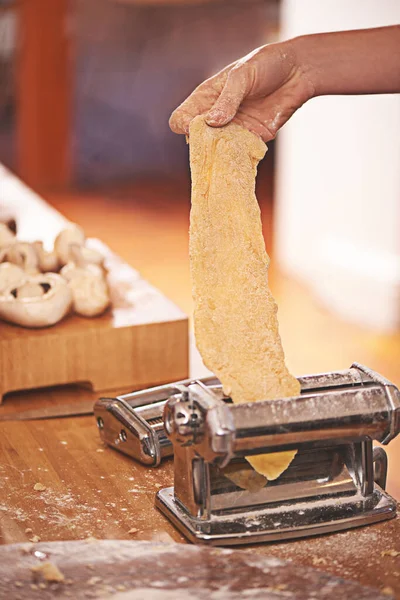 Паста ла виста. Обрезанный снимок человека, скатывающего свежеприготовленное тесто через изготовитель макарон. — стоковое фото