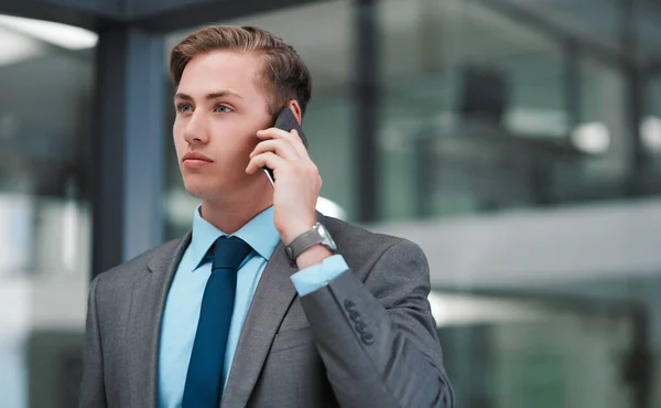 Det meste av virksomheten min er gjort på telefonen. Sprengt bilde av en kjekk, ung forretningsmann som står alene på kontoret og bruker mobilen sin. – stockfoto