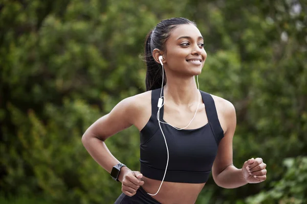 I know where Im going. Shot of a sporty young woman wearing earphones while running outdoors. — Stock Photo, Image