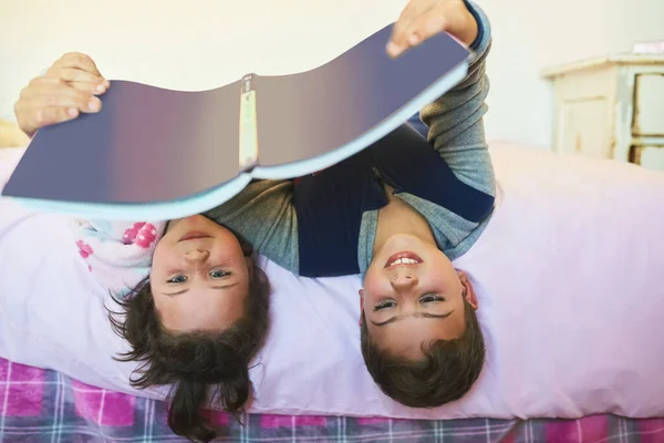 Sdílejí lásku ke čtení. Vystřižený záběr dvou mladých sourozenců, jak spolu čtou knihu, zatímco leží hlavou dolů na posteli. — Stock fotografie