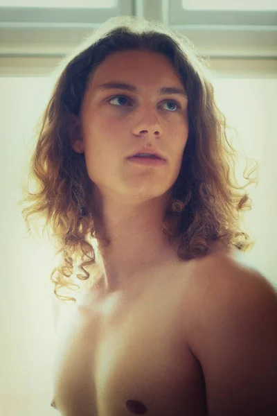 Ha uno sguardo intenso. Un giovane bell'uomo senza maglietta in piedi accanto a una finestra. — Foto Stock