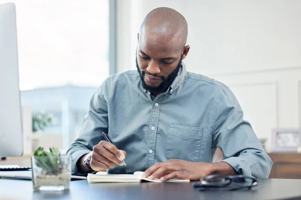 La pianificazione è essenziale per raggiungere gli obiettivi. Girato di un bel giovane uomo d'affari seduto da solo in ufficio a scrivere nel suo taccuino. — Foto Stock