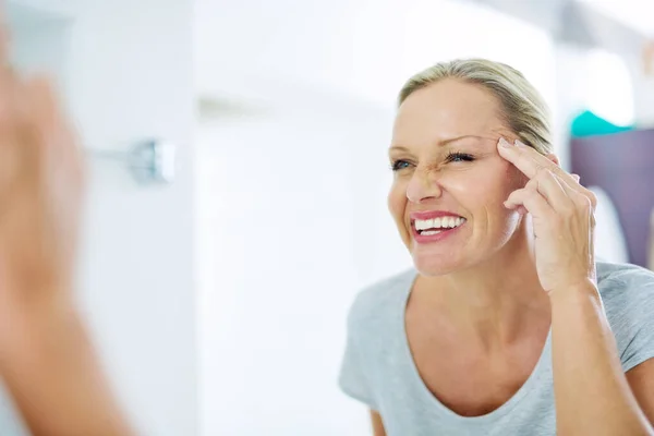 Door goede huidverzorgingsgewoonten zie je er jonger uit. Gesneden schot van een volwassen vrouw inspecteren haar huid in de voorkant van de badkamer spiegel. — Stockfoto