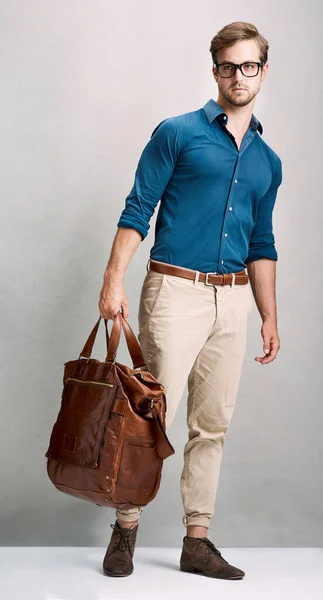 Viajando em grande estilo. Retrato de comprimento total de um jovem bonito posando com um saco no estúdio. — Fotografia de Stock