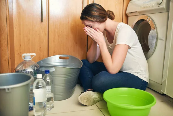 Sentirse estresado por la crisis del agua. Foto de una hermosa joven llorando en el suelo en la cocina en casa. — Foto de Stock