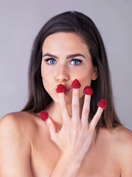 Que bom. Estúdio retrato de uma jovem mulher atraente comendo framboesas fora de seus dedos contra um fundo roxo. — Fotografia de Stock