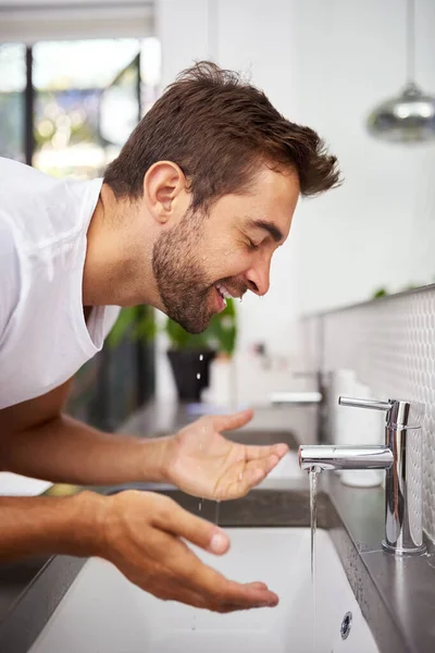 A sensação refrescante de um rosto limpo. Close up tiro de um homem bonito lavar o rosto na casa de banho em casa. — Fotografia de Stock