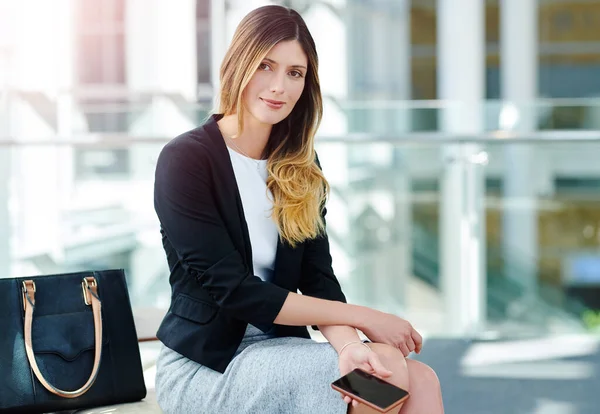 Först och främst måste du vara affärsmässig. Beskärda porträtt av en attraktiv ung affärskvinna som håller en smartphone sittande i ett väntrum. — Stockfoto