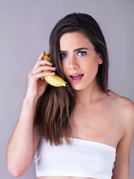 Posso estar a enlouquecer porque não te consigo ouvir. Retrato de estúdio de uma jovem atraente fingindo usar uma banana como um telefone contra um fundo roxo. — Fotografia de Stock
