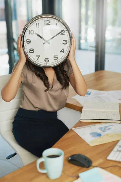 Elle a du temps à perdre. Prise de vue d'une femme d'affaires non identifiable tenant une horloge devant son visage assis à son bureau. — Photo