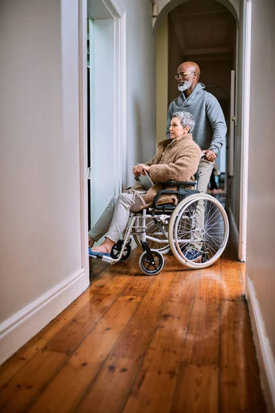 Pomagam jej się poruszać. Przycięte ujęcie starszego mężczyzny pchającego żonę na wózku inwalidzkim przez dom. — Zdjęcie stockowe