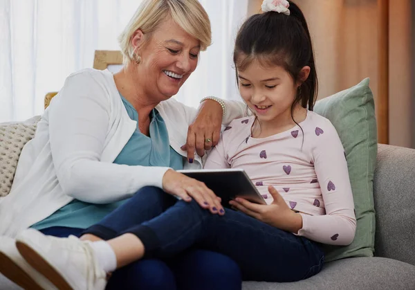 Deixa-me ver a tua pontuação... Tiro de uma menina adorável usando um tablet digital enquanto sentada em casa com sua avó. — Fotografia de Stock
