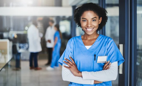 Rien ne me rend plus heureux que de voir mes patients en bonne santé. Portrait d'une jeune médecin confiante travaillant dans un hôpital avec ses collègues en arrière-plan. — Photo