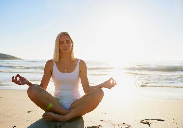 Namaste juste ici. Plan complet d'une jolie jeune femme assise les jambes croisées et méditant sur la plage. — Photo