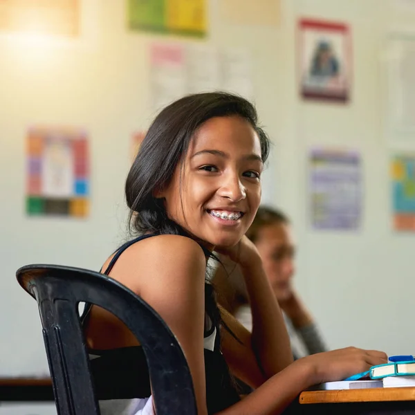 Эта школа супер классная. Портрет счастливой молодой школьницы, оглядывающейся через плечо в классе. — стоковое фото