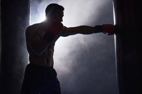 Pracuju na jeho technice. Vystřižený záběr siluety mladého mužského boxera cvičit na boxovací pytel v tělocvičně. — Stock fotografie