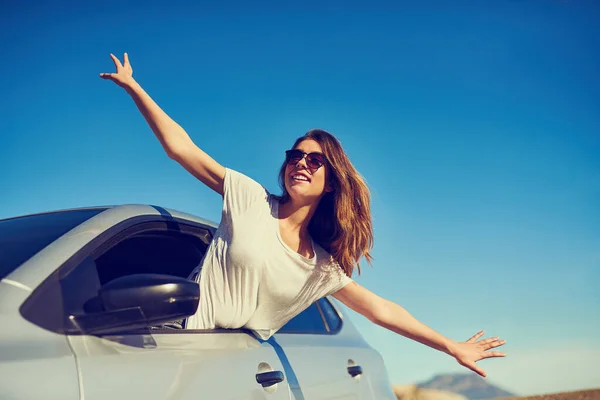 Total freedom. Shot of a young woman leaning out of her car window with her arms outstretched.