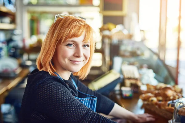 Je zult hier altijd service krijgen met een glimlach. Portret van een zelfverzekerde jonge vrouw die in een koffieshop werkt. — Stockfoto