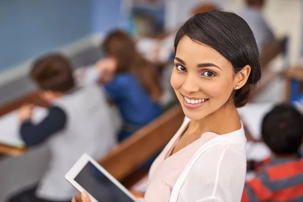 Unterrichten auf moderne Weise. Porträt einer glücklichen jungen Lehrerin mit einem Tablet im Hintergrund. — Stockfoto