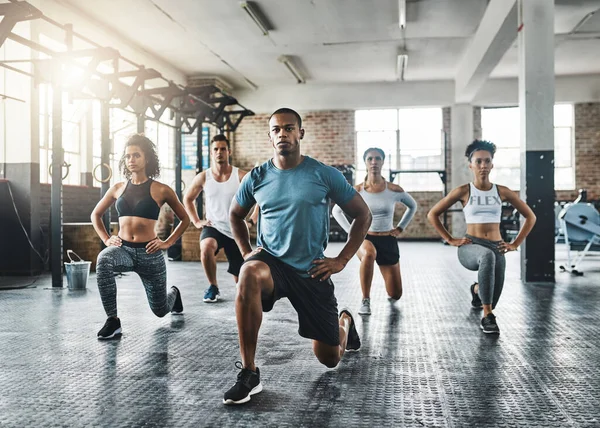 Varje steg mot kondition lönar sig. Skjuten av en grupp ungdomar som gör lungor tillsammans under sin träning i ett gym. — Stockfoto