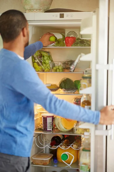 Buzdolabı sağlıklı beslenmeyi teşvik ediyor. Evde sağlıklı yiyeceklerle dolu buzdolabını açan bir adamın dikiz görüntüsü.. — Stok fotoğraf