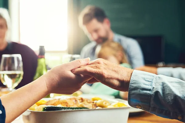Semuanya berpegangan tangan. Penutup dari keluarga yang damai berpegangan tangan untuk mengucapkan kasih karunia bersama-sama di sekitar meja makan di rumah. — Stok Foto