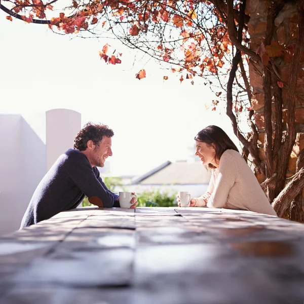 Partilhar histórias à luz do sol. Um casal sentado em uma mesa de madeira sob as folhas de outono. — Fotografia de Stock