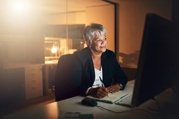 Als het de moeite waard is, werk er dan voor. Foto van een volwassen zakenvrouw die schrijft in een notitieboekje en een computer gebruikt tijdens een late avond op het werk. — Stockfoto