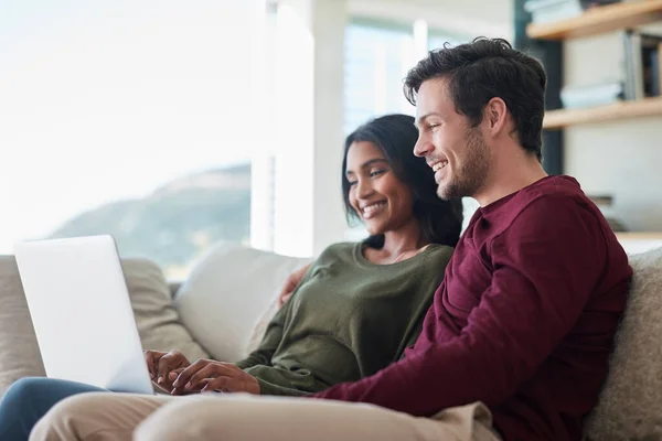 Ils ont mis le "nous" le week-end. Prise de vue d'un jeune couple affectueux utilisant leur ordinateur portable assis sur le canapé à la maison. — Photo