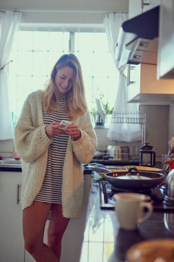 Lunch is ready, where are you. Cropped shot of an attractive young woman texting on a cellphone while cooking in her kitchen. clipart