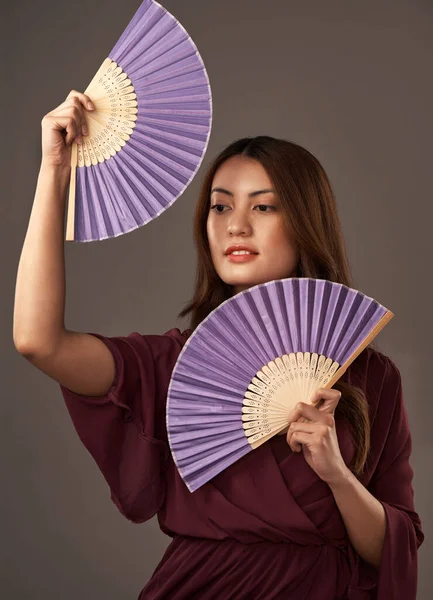 Its a tradition. Cropped portrait of an attractive young woman posing with fans in studio against a grey background.