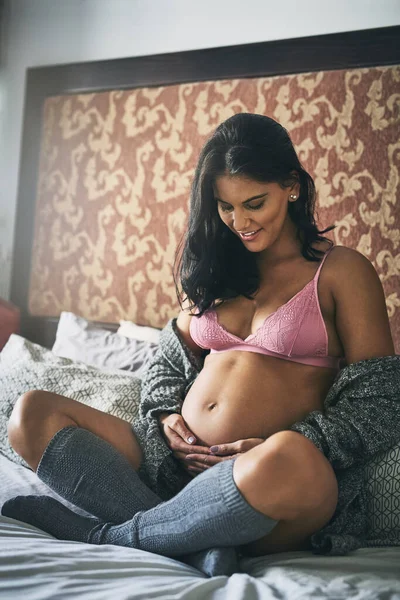 Może powiedzieć swoim dzieciom, że będą zdrowe. Całkowite ujęcie atrakcyjnej, młodej kobiety w ciąży siedzącej na łóżku w domu. — Zdjęcie stockowe