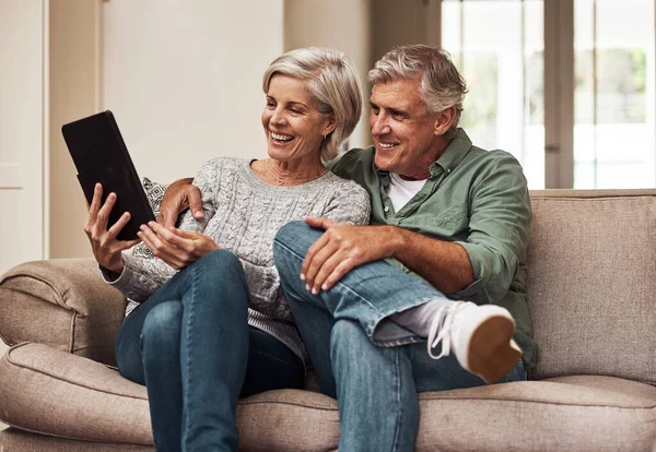 On ne connaît plus la télé. Plan recadré d'un couple de personnes âgées joyeux naviguant sur une tablette numérique ensemble tout en étant assis sur un canapé à la maison pendant la journée. — Photo
