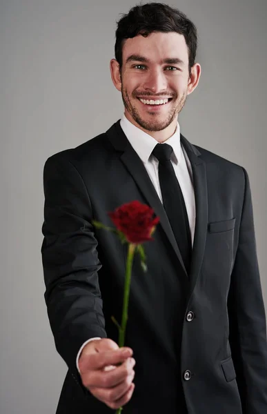 Den perfekta gentlemannen. Studio skott av en välklädd man som håller en röd ros mot en grå bakgrund. — Stockfoto