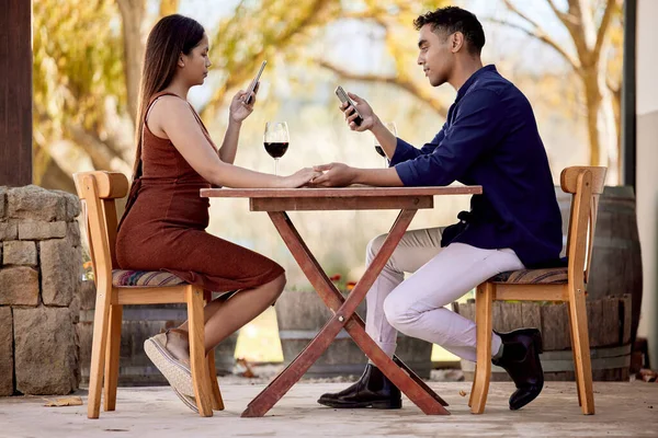 Bébé, juste une seconde. Je dois mettre à jour mes relations sociales. Tournage d'un jeune couple qui boit du vin à un rendez-vous dans une exploitation viticole. — Photo