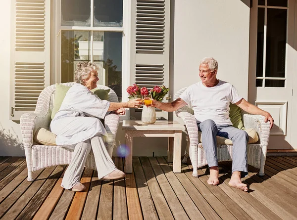Hay más mañanas como esta. Foto de una feliz pareja de ancianos brindando con jugo en el patio en casa. — Foto de Stock