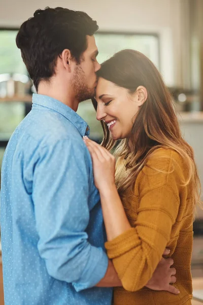 Var tillsammans för evigt. Skjuten av en kärleksfull ung man kysser sin flickvän i pannan i deras kök. — Stockfoto