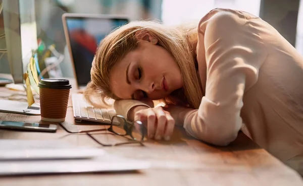 Longas horas estão a cobrar o preço. Tiro de uma jovem empresária exausta dormindo em sua mesa em um escritório. — Fotografia de Stock