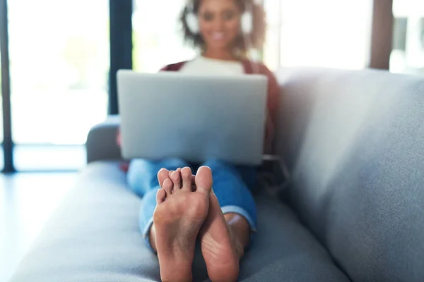 Розслаблені ноги щасливі ноги. Постріл молодої жінки за допомогою навушників і ноутбука на дивані вдома . — стокове фото