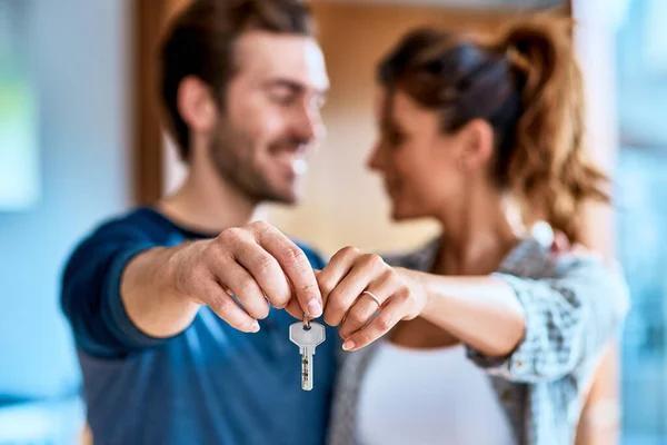 Le chiavi della nostra nuova casa. Girato di una giovane coppia allegra che tiene insieme una chiave per la loro nuova casa mentre in piedi all'interno durante il giorno. — Foto Stock