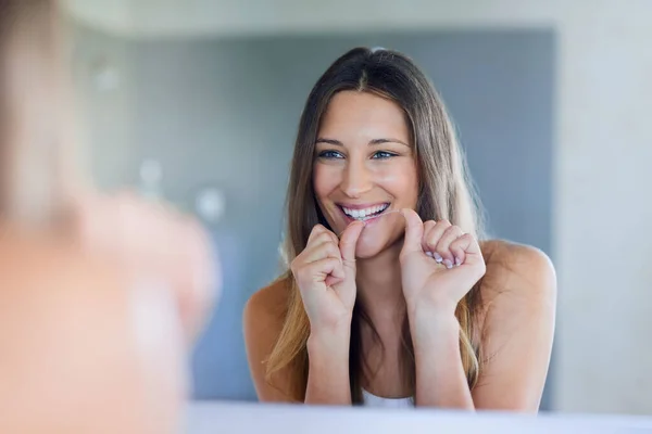 Making sure she cleans every nook and cranny. Shot of a happy young woman using dental floss to clean her teeth at home. — Stock Photo, Image