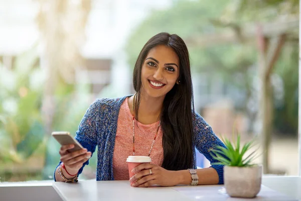Ich komme wegen des Wifi, aber auch wegen des Kaffees. Porträt einer attraktiven jungen Frau, die ihr Handy benutzt, während sie in einem Café Kaffee trinkt. — Stockfoto