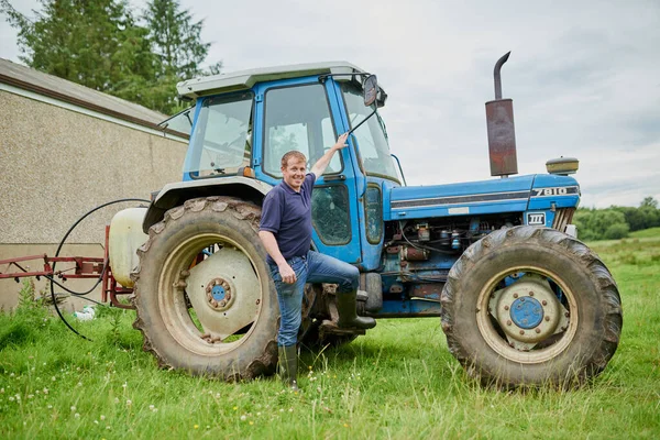 Pojďte se podívat do mé kanceláře. Portrét veselého mladého farmáře pózujícího vedle svého velkého farmářského traktoru venku na poli. — Stock fotografie