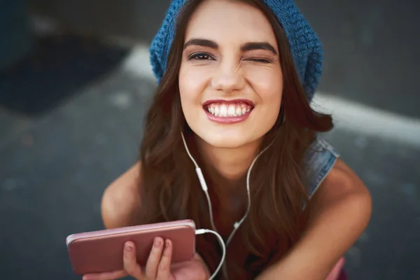 Elle a trouvé la bonne chanson pour l'occasion. Portrait d'une jeune femme insouciante assise sur le sol tout en écoutant de la musique à travers ses écouteurs à l'extérieur pendant la journée. — Photo