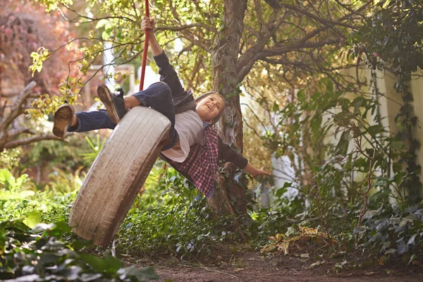 Zorgeloze zomerdagen van een idyllische jeugd. Een knappe jongen swingend op een band schommel in de tuin. — Stockfoto