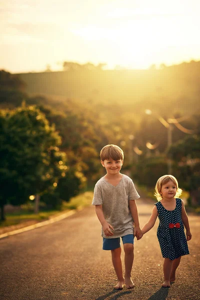 Su hermano mayor siempre la acompaña a donde quiera que vaya. Un disparo de un adorable hermanito y hermana dando un paseo por el camino juntos afuera. — Foto de Stock