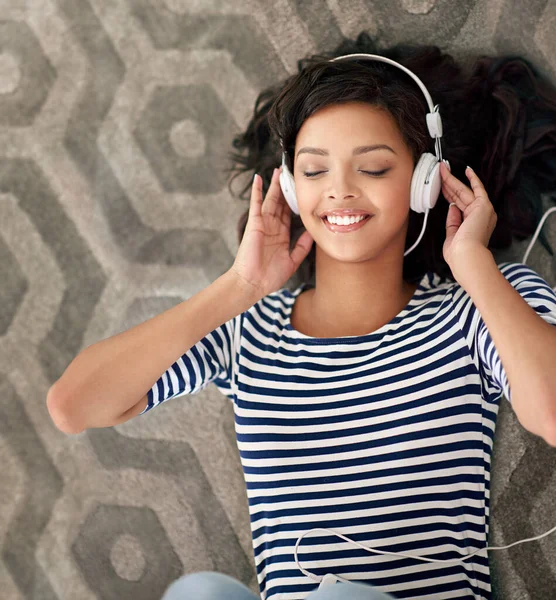 Sladké zvuky hudby. Vysoký úhel záběr mladé ženy, jak poslouchá hudbu na mobilním telefonu, zatímco leží na podlaze. — Stock fotografie