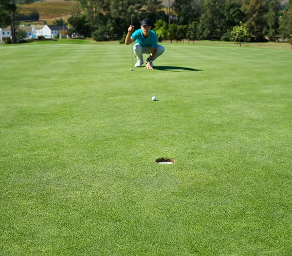 Ça a l'air facile. Tourné d'un jeune homme concentré attendant la balle de golf qu'il vient de frapper pour aller dans un trou à l'extérieur sur un terrain de golf. — Photo