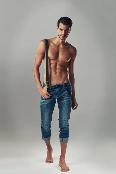 Набирання статі. Студійний знімок красивого молодого чоловіка в джинсах і підтяжках на сірому фоні . — стокове фото