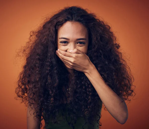 Sto cercando di non ridere. Colpo di una donna con i capelli ricci che si copre la bocca mentre ride su uno sfondo arancione. — Foto Stock